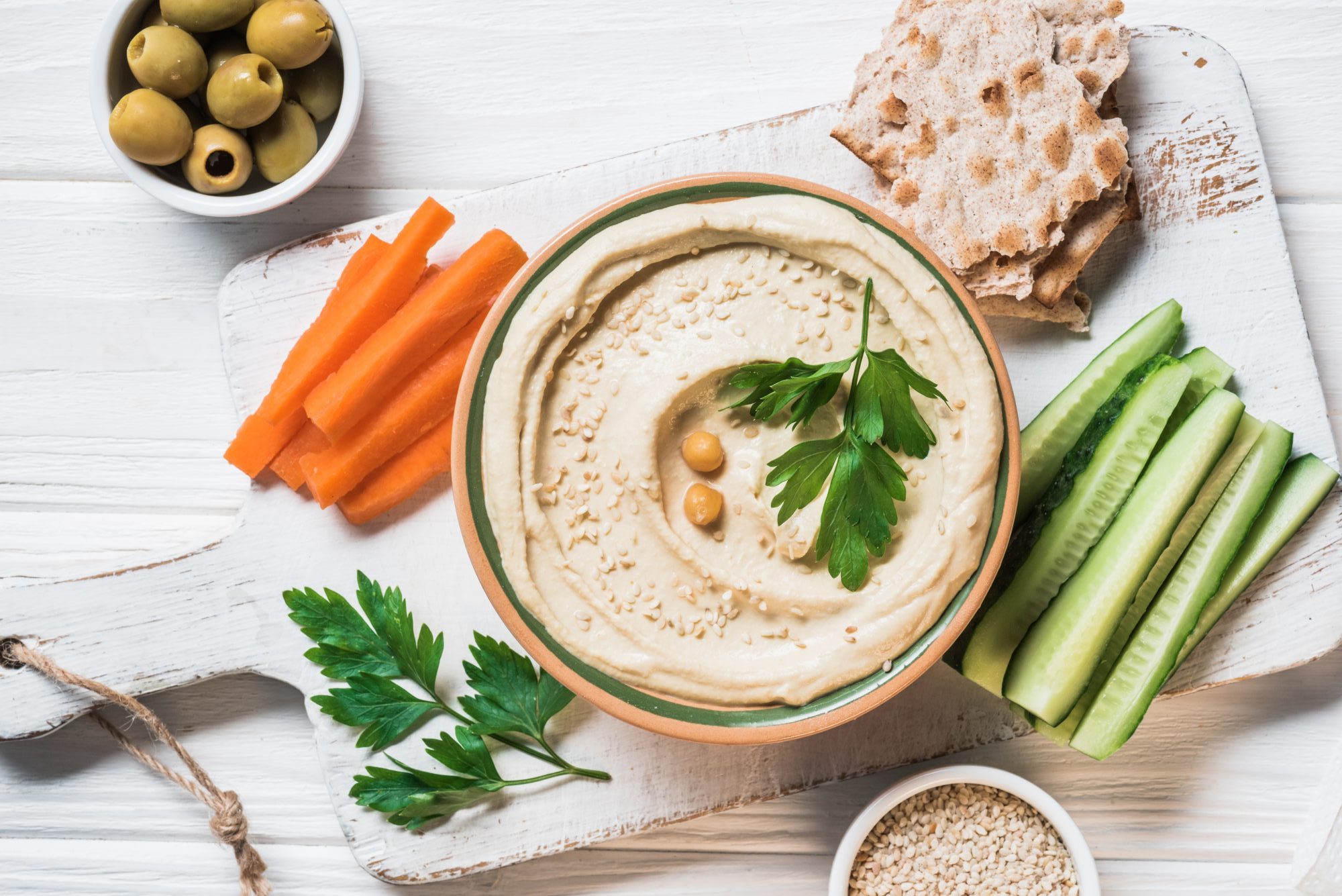 top view of hummus with parsley, cut vegetables and pita bread on wooden tabletop